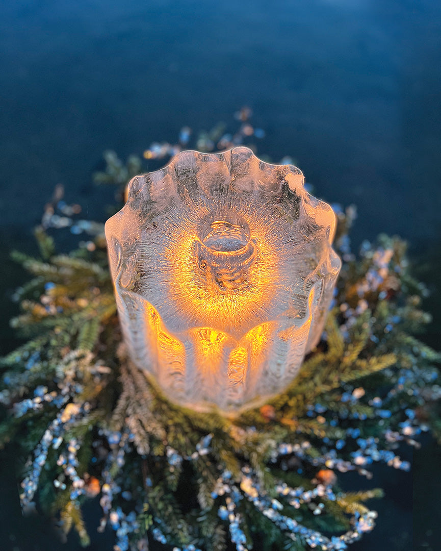A fluted ice lantern in a nest of sparkly greens and lit with a candle - view from above 